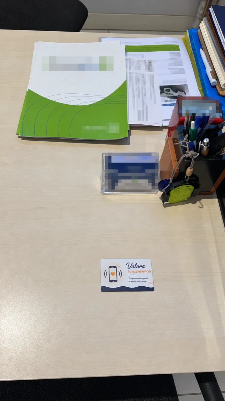 Mesa de un vendedor en una compraventa de coches, con la tarjeta NFC «Valora tu experiencia» delante
