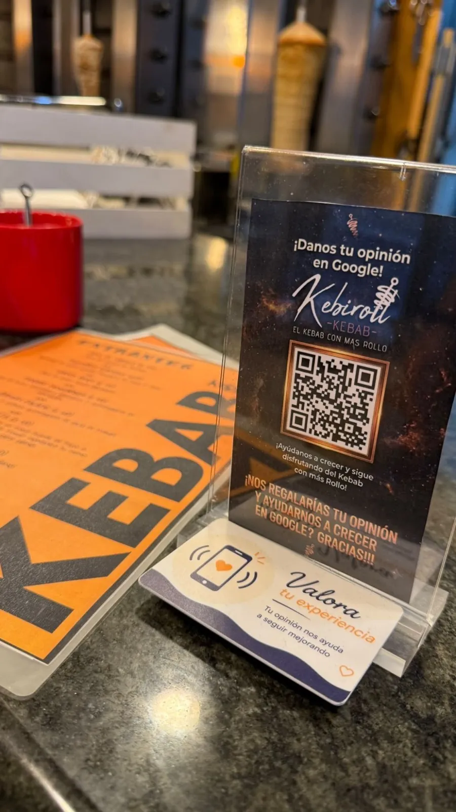 Tarjeta NFC «Valora tu experiencia» apoyada en un expositor, en el mostrador de un kebab de Ponteareas
